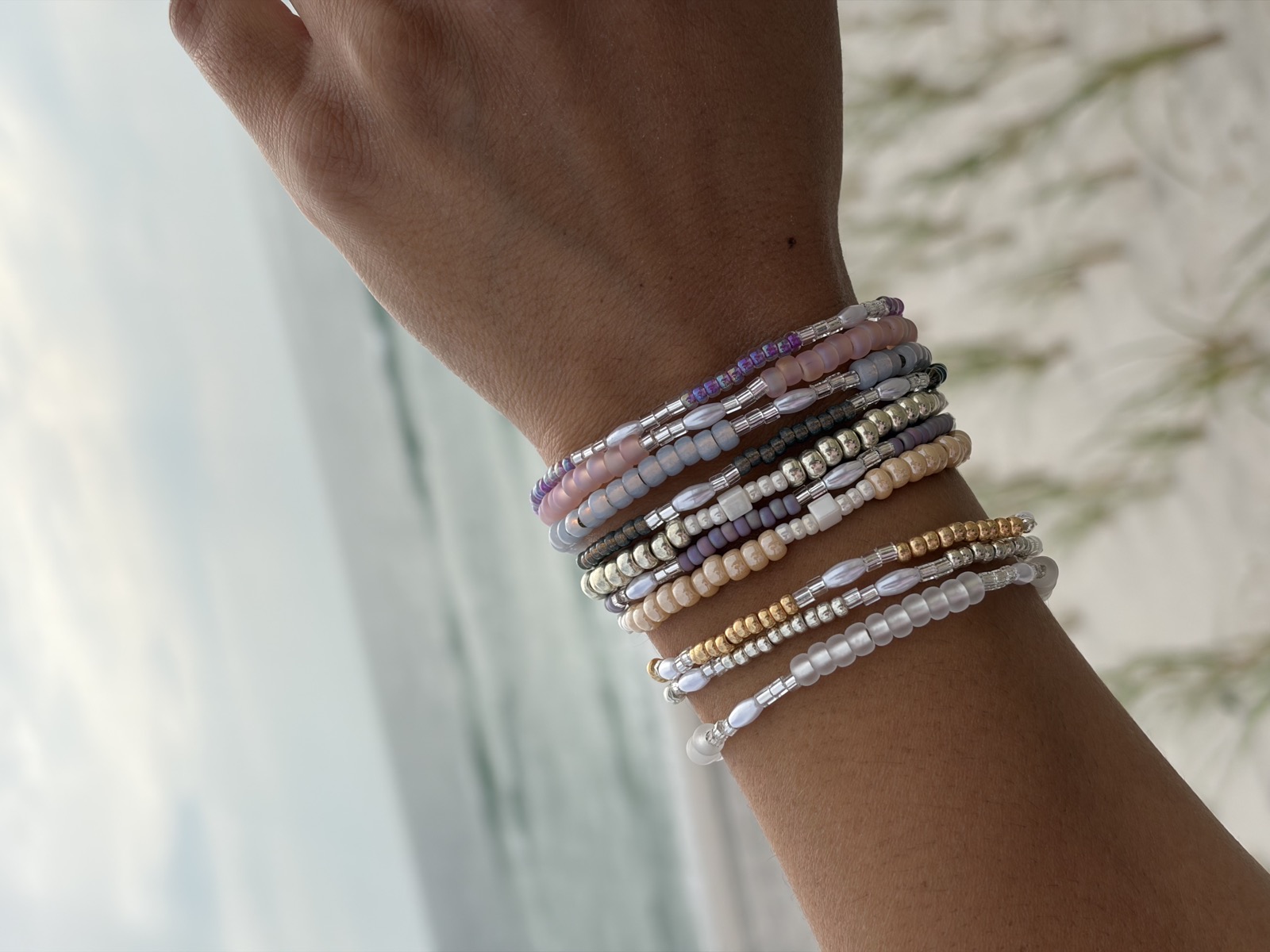 A stack of handmade beaded stretch bracelets on a wrist at the beach